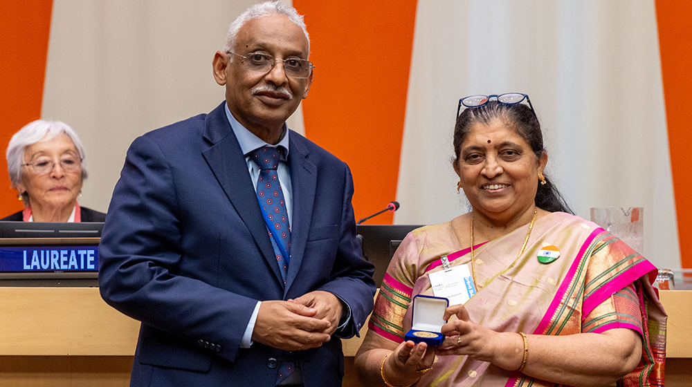 A man and a woman smile and pose with a medal in hand