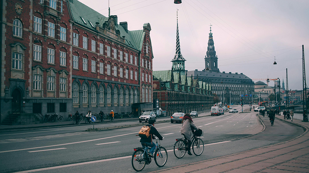Cyclists riding along a wide embankment near historic buildings in Copenhagen city