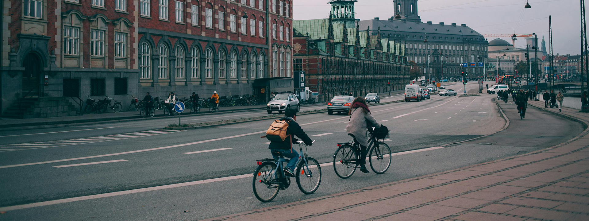 Cyclists riding along a wide embankment near historic buildings in Copenhagen city