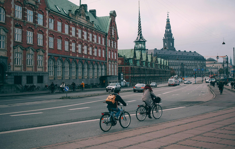 Cyclists riding along a wide embankment near historic buildings in Copenhagen city