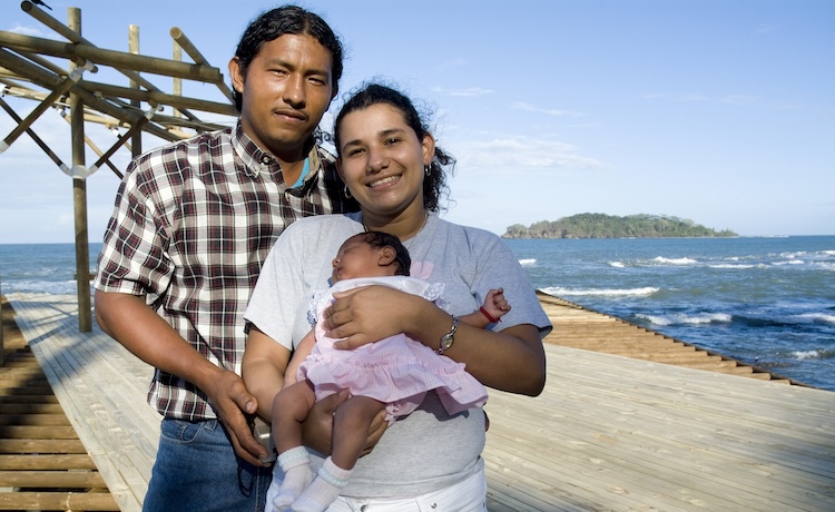 A father and mother hold their infant in their arms. 