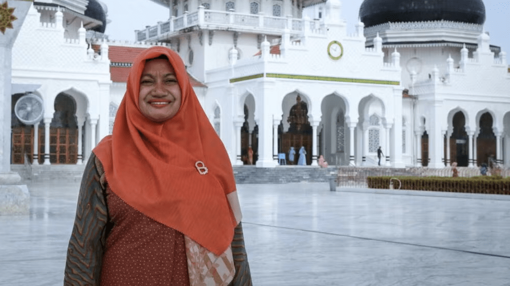 The photo shows Nurlinawati standing in front of a building.