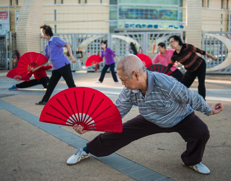 A group of elderly people perform with colourful fans.