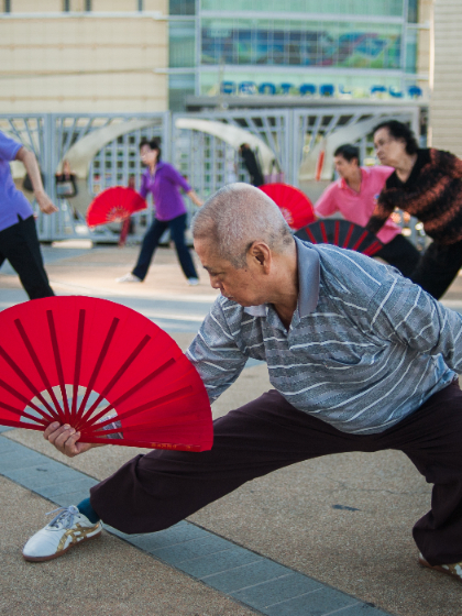 A group of elderly people perform with colourful fans.