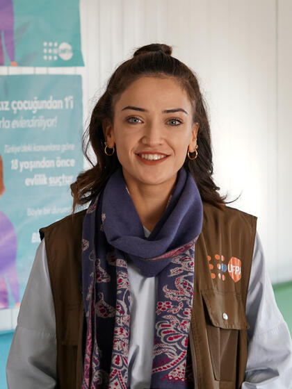 A Social Services Expert wears a vest with a UNFPA logo and stands in a class room setting. 